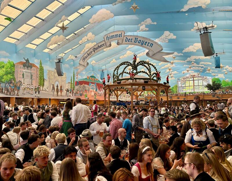 Inside the Hacker-Festzelt at Oktoberfest: long benches full of people in Tracht under a painted blue sky ceiling.